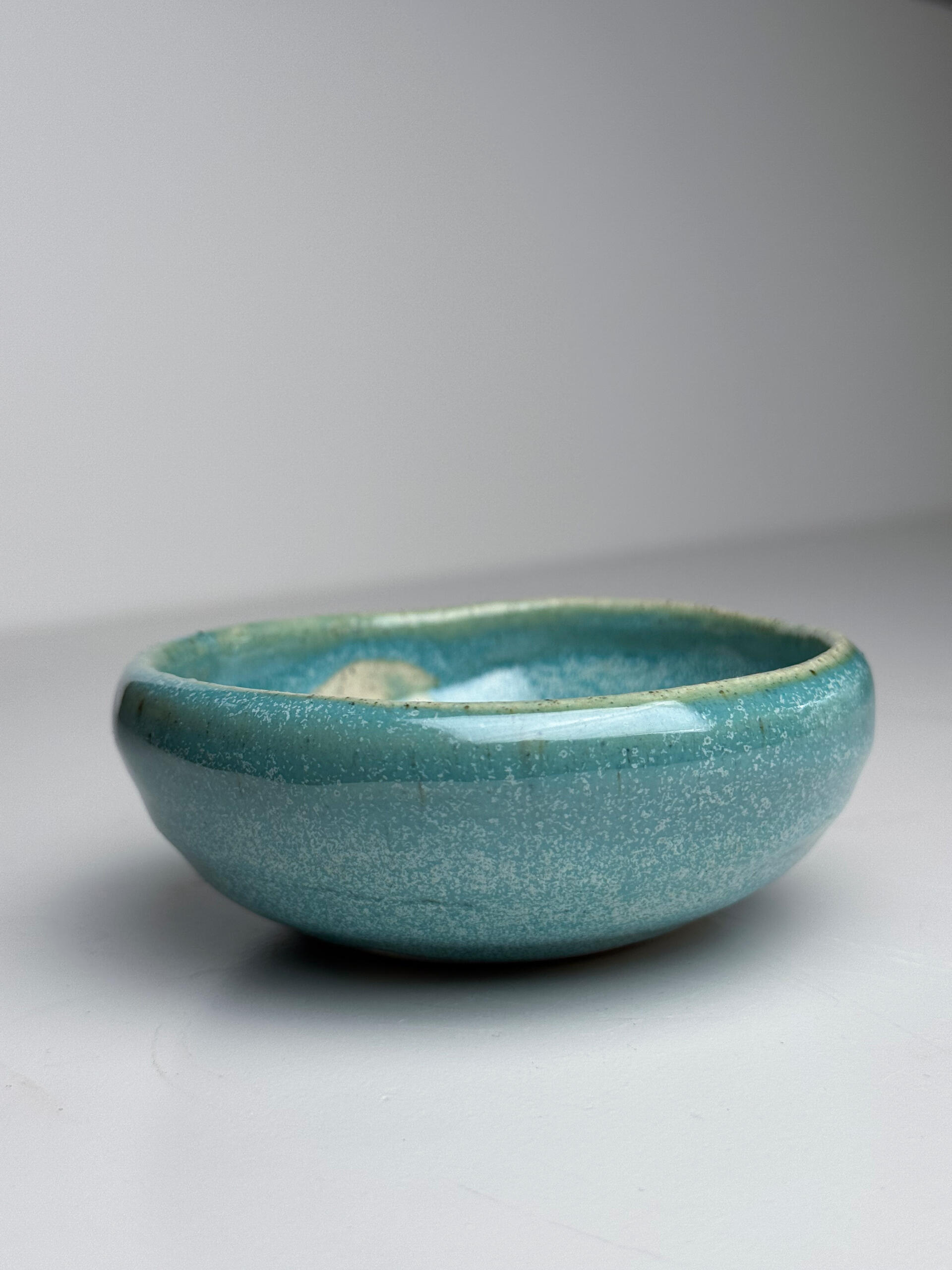 Blue-gre Gradient Bowl Small handmade ceramic bowl with flowing blue glaze over natural clay base, sitting on a white surface