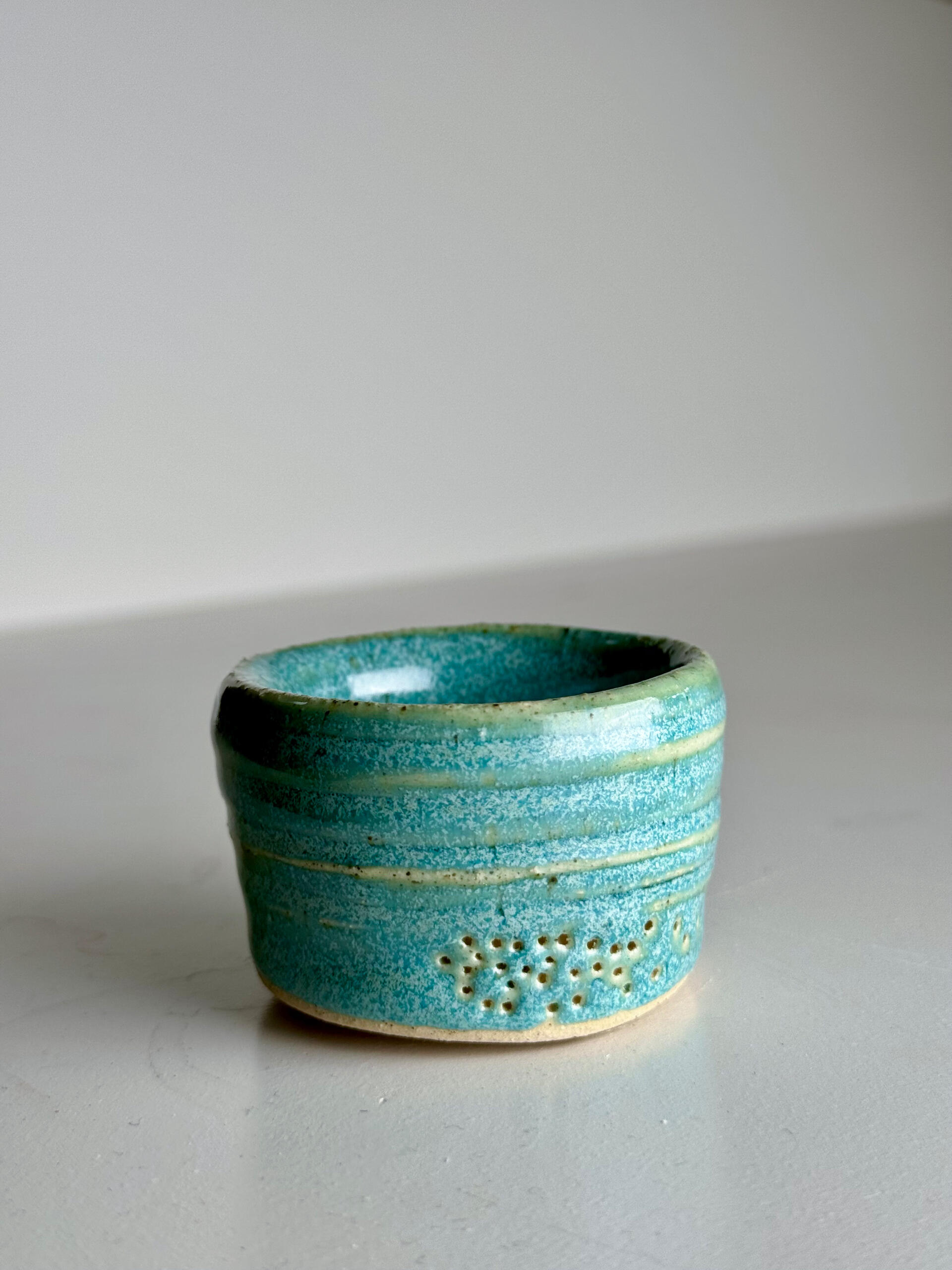 Green-Blue Cup Small handmade ceramic cup with flowing green-blue over natural clay base, sitting on a white surface
