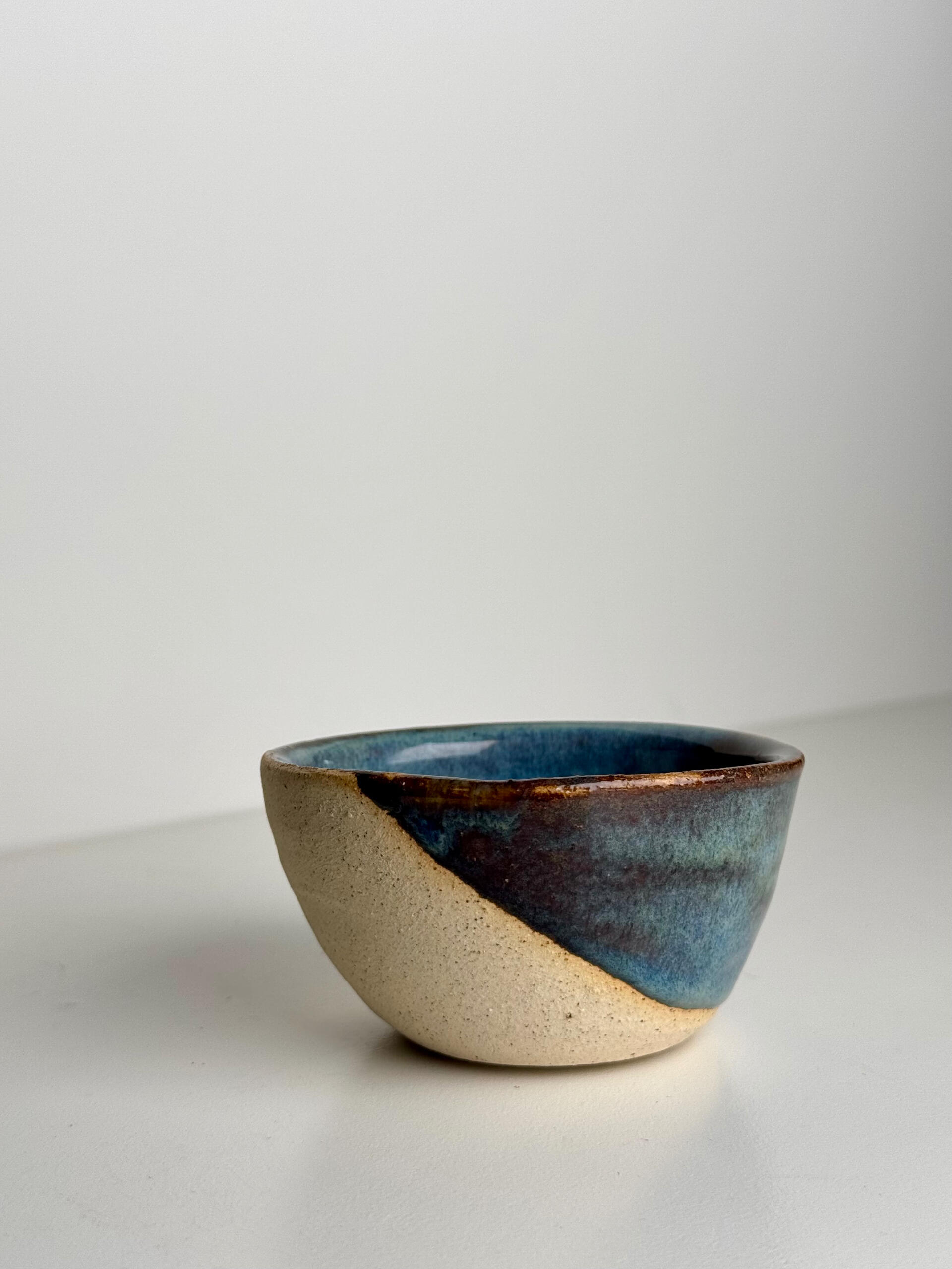 Blue Gradient Cup Small handmade ceramic cup with flowing blue glaze over natural clay base, sitting on a white surface